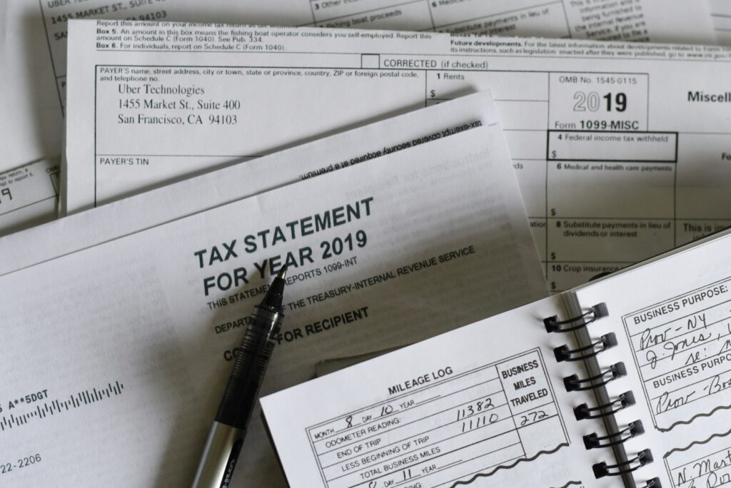 A pen resting on tax forms and a mileage log book, representing a tax return