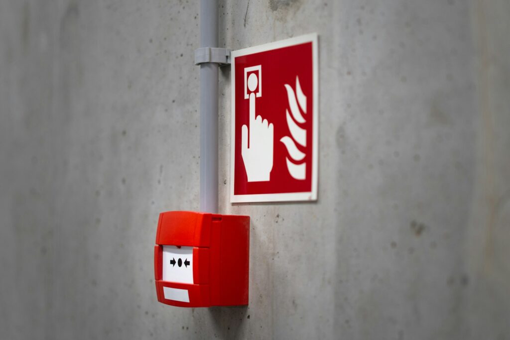 A red fire alarm call point mounted on a concrete wall, ready to be triggered