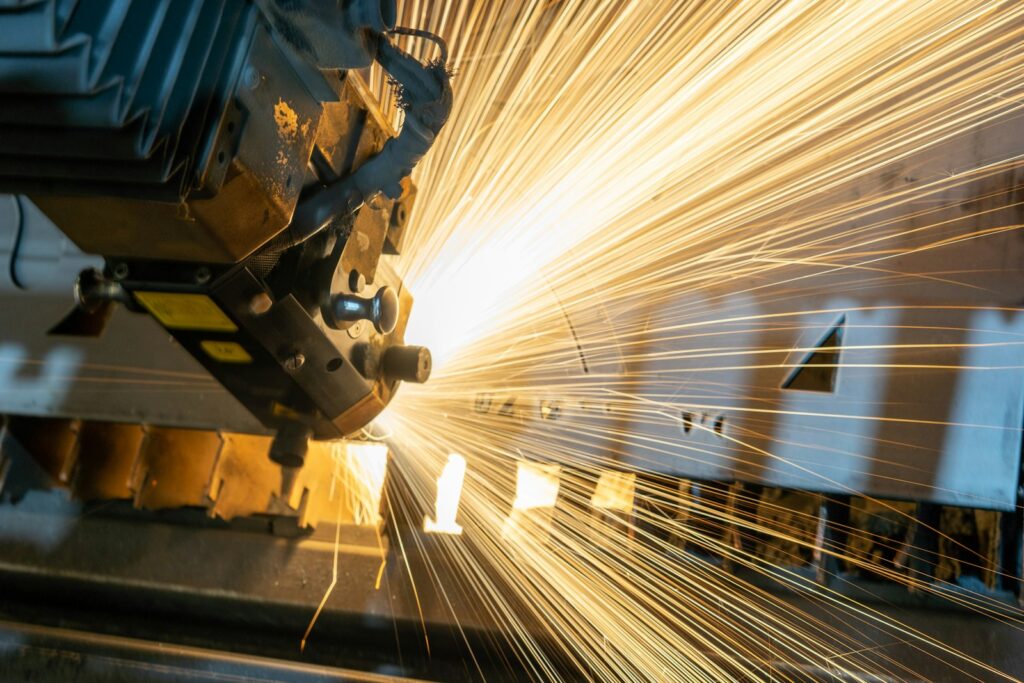 A laser cutting machine throwing bright orange sparks as it slices through a metal sheet